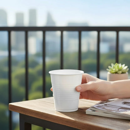 Food Packaging Direct 7oz white disposable plastic water cup held on a balcony table with a city skyline background